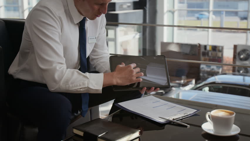 Close up shot of unrecognizable car salesman holding tablet and pointing at screen while explaining car specifications to client during consultation in dealership, copy space