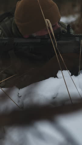 Soldier on a military recon mission in the wilderness. Frozen forest full of snow at winter. Hiding in the snow and aiming