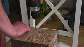Man in casual clothes drilling deep hole into wooden beam with cordless drill creating sawdust at home with plants in background. Concept of weekend DIY project, woodcraft hobby and handyman skills. - Powered by Shutterstock - Get 15% off with code: PIKWIZARD15