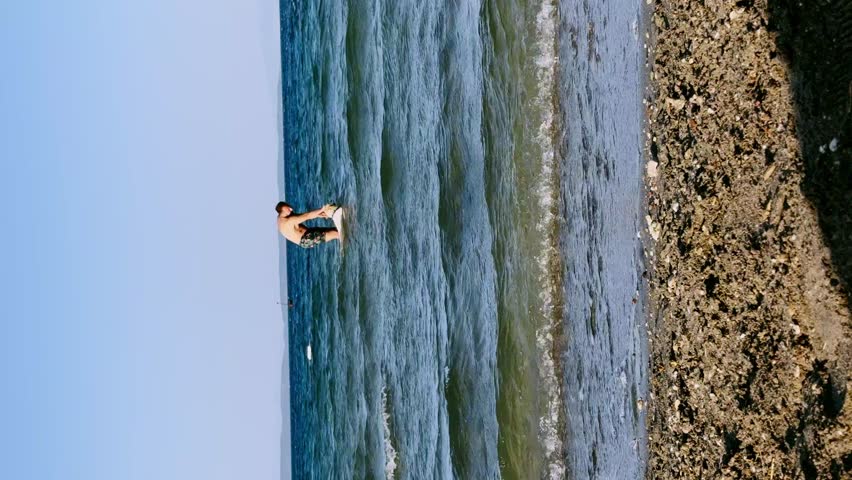 30s man playing fetch with Golden Retriever at beach, dog retrieves toy from ocean then shakes off water

