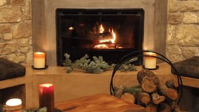 A detailed 4K view of a cozy, lit fireplace with logs burning behind glass doors, rustic stone accents, and two large, lit candles. - Powered by Shutterstock - Get 15% off with code: PIKWIZARD15