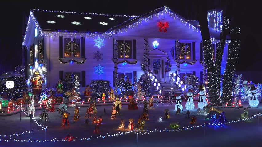 A detailed 4K view of a house extensively decorated with bright Christmas lights and various holiday-themed decorations at night.