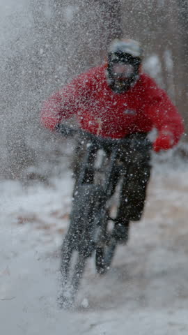 SLOW MOTION, DOF, CLOSE UP: MTB rider racing and drifting down the snowy trail. Freshly fallen snow is flying around as adrenaline seeking biker rides fast along forest path on a cold winter day.