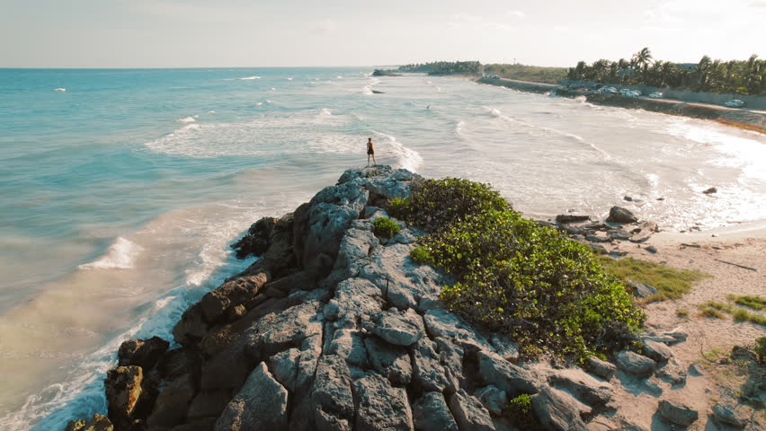 Lone figure of woman on rocky outcrop with ocean and beach in view in Mexico