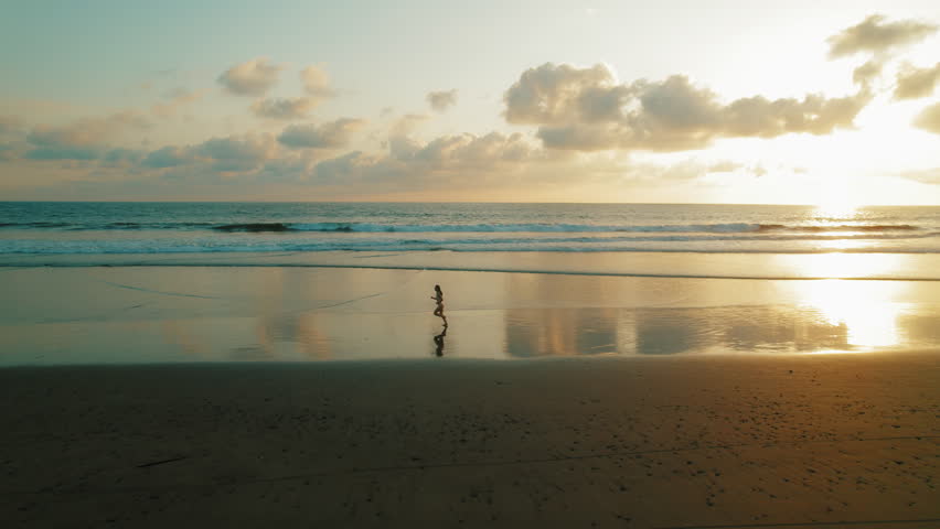 Woman running along beach at sunset reflected on wet black sand in Costa Rica