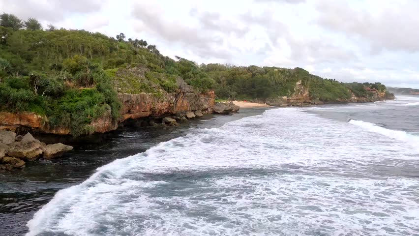 A scenic coastal landscape with waves crashing against a rocky shoreline, surrounded by lush greenery and cliffs under a cloudy sky. Perfect for travel brochures, nature documentaries