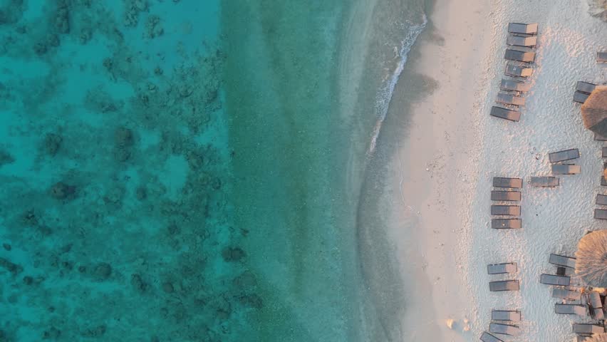 Top-down aerial view of a tropical resort with pools, palm trees, and beachfront cabanas situated above clear turquoise waters and a peaceful sandy shore.