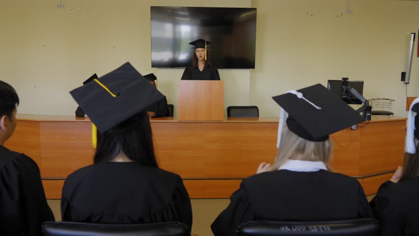 A young woman stands at the lectern and delivers a graduation speech to her classmates. 