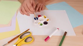 Person mixes watercolor paints on palette with brush, surrounded by art supplies under bright lighting - Powered by Shutterstock - Get 15% off with code: PIKWIZARD15