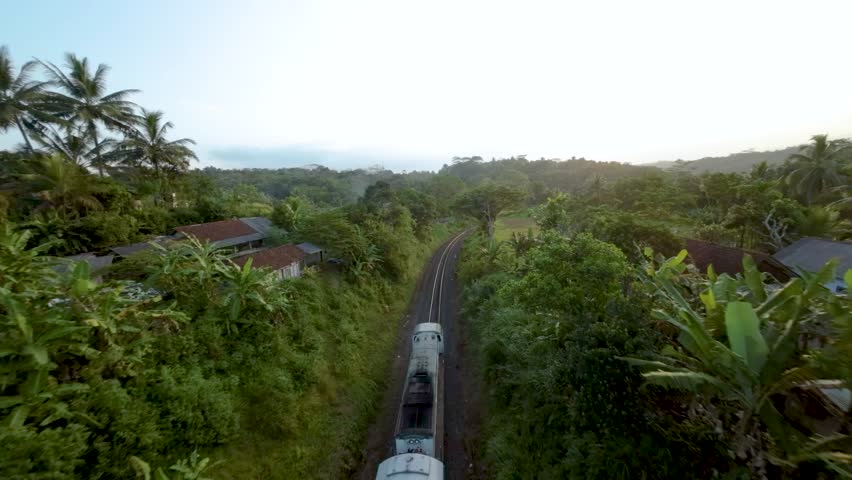 High-Speed FPV Drone Tracking Shot of a Train Approaching a Sharp Curve in a Lush, Green Valley Landscape