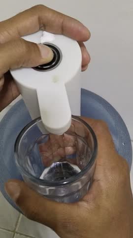 hand filling a glass with clean water using a white portable electric gallon pump. Practical and hygienic solution for everyday drinking water