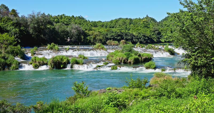 Beautiful river rapids and small waterfalls with lush green forest in Guizhou, China.