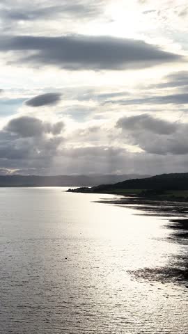 Small boat moves across tranquil water under dramatic sunset clouds, sunbeams, and reflective surface