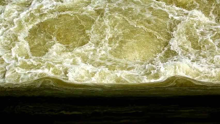 Rushing water flowing rapidly creating turbulent waves and foam from above view