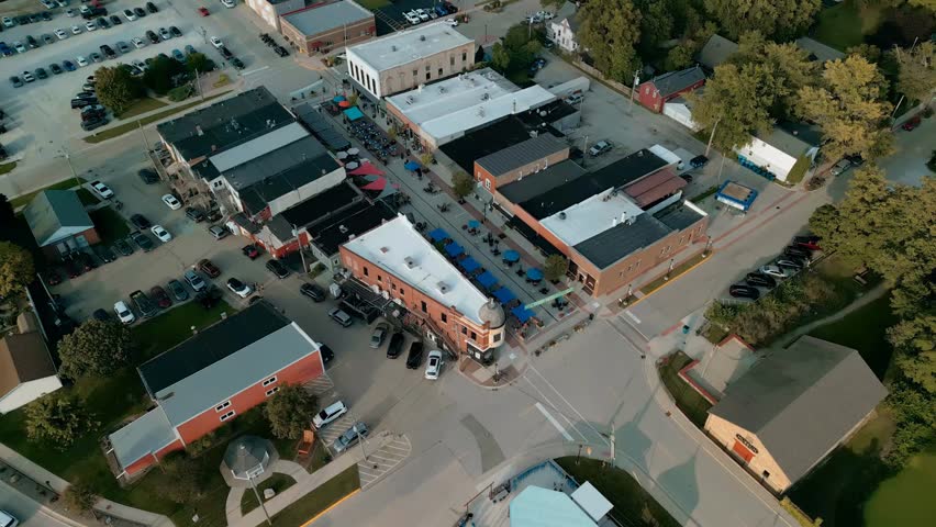 Aerial view of small town houses glowing in warm golden hour light, showing peaceful residential patterns, rooftops, and calm neighborhood scenery from above.