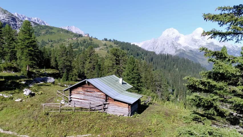 Rustic cabin nestled in the alps with snow capped mountains and green forest view