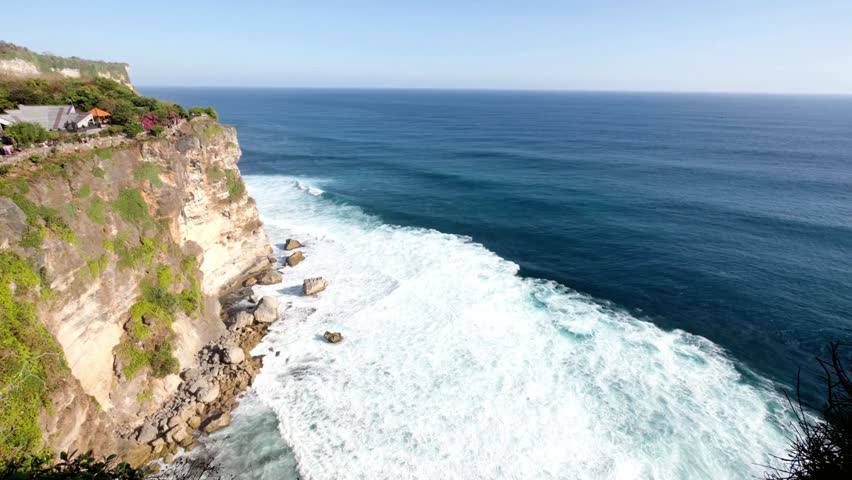 Cliffside view of ocean waves crashing against the shore on a sunny day in bali