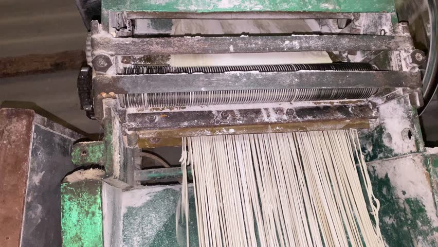 Industrial noodle-making machine rolling and cutting fresh dough in a fast, automated process. Perfect for food production, factory workflow, and manufacturing footage.