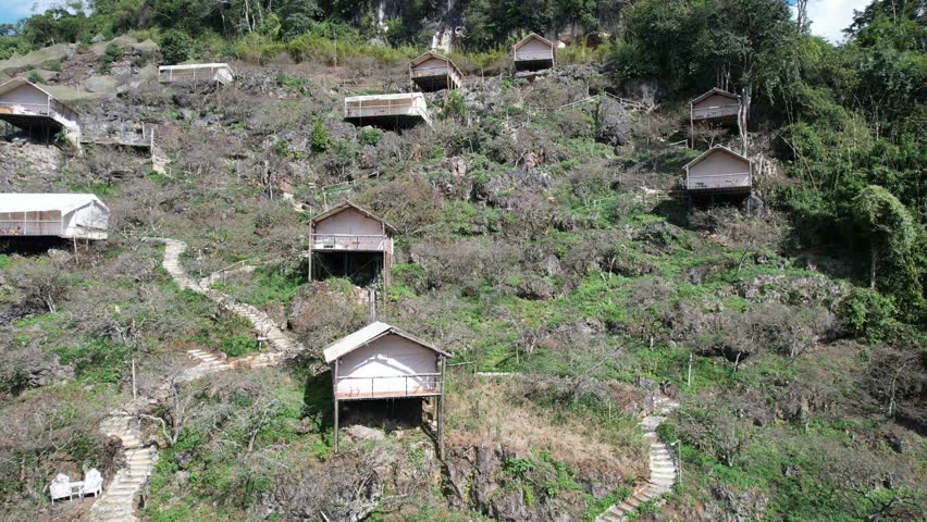 Drone panning shot sweeping from right to left across the white tent-style homestay area on the karst mountain slope of Mu Nau, Moc Chau, showcasing the rugged highland scenery.