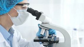 Female scientist analyzing research sample through microscope, wearing protective lab gear for medical investigation. Laboratory and science concept - Powered by Shutterstock - Get 15% off with code: PIKWIZARD15