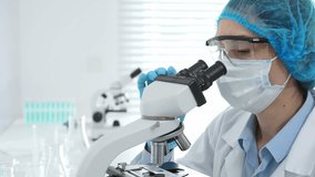 Female scientist analyzing sample through microscope, wearing protective lab gear during medical research investigation. Medicine, laboratory and science concept - Powered by Shutterstock - Get 15% off with code: PIKWIZARD15