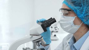 Female scientist analyzing sample through microscope, wearing protective lab gear during medical research investigation. Medicine, laboratory and science concept - Powered by Shutterstock - Get 15% off with code: PIKWIZARD15