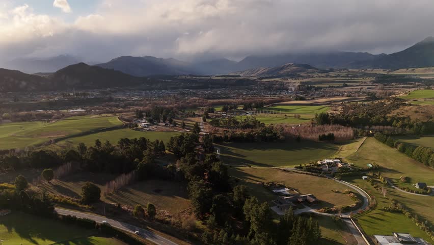 Scenic city of wanaka and driving cars on rural road in suburb during sunset time. Aerial wide shot. Colored autumnal evening in New Zealand.