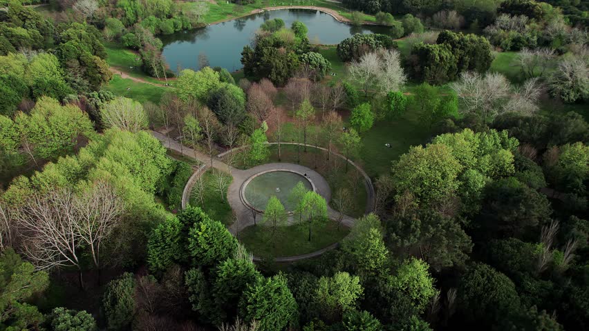 Orbiting drone shot captures an elaborate circular fountain or paved structure surrounded by a pathway, nestled deep within the lush forest of the Parque da Cidade do Porto, Portugal