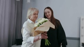 Senior woman warmly receiving white roses bouquet from young granddaughter, expressing loving connection and heartfelt moment of family affection indoors - Powered by Shutterstock - Get 15% off with code: PIKWIZARD15