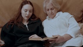 Elderly grandmother and young granddaughter lying closely on soft sofa, sharing intimate reading moment with deep familial connection and educational interaction - Powered by Shutterstock - Get 15% off with code: PIKWIZARD15