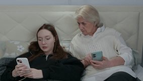 Elderly grandmother and teenage granddaughter sharing digital moment, bonding through smartphone interaction while sitting comfortably on bed, representing modern family connection - Powered by Shutterstock - Get 15% off with code: PIKWIZARD15