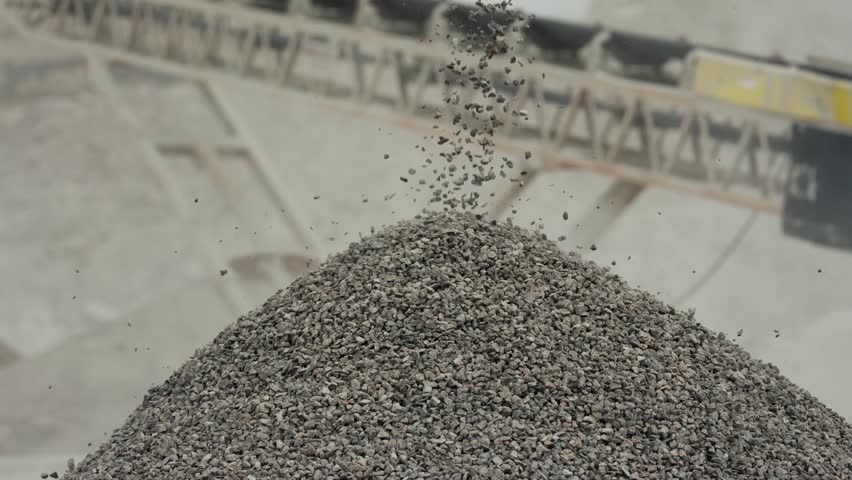 Handheld cinematic shot of gravel flowing off a conveyor belt at a mining crushing site, capturing industrial machinery, material processing, and rugged textures.