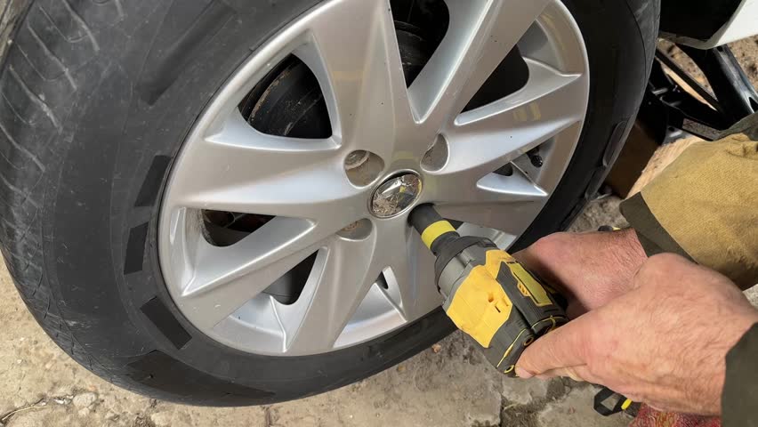 Cordless impact wrench loosens a lug nut on a car wheel, medium angle view