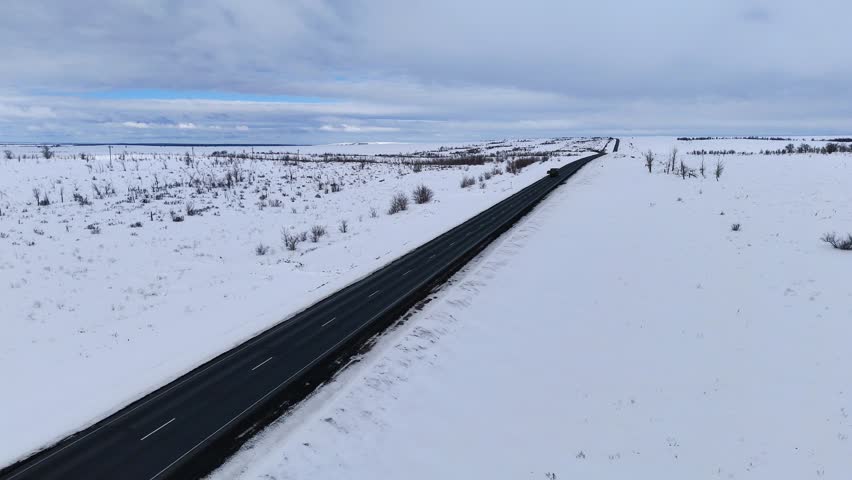trucks and cars drive along the highway in the winter, through snow-covered fields