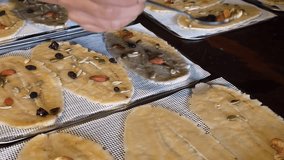 process of making a healthy snack, where a person's hand uses a small spoon to distribute various nuts, seeds, and dried fruits onto slices of flattened or dried banana. The slices are arranged  - Powered by Shutterstock - Get 15% off with code: PIKWIZARD15