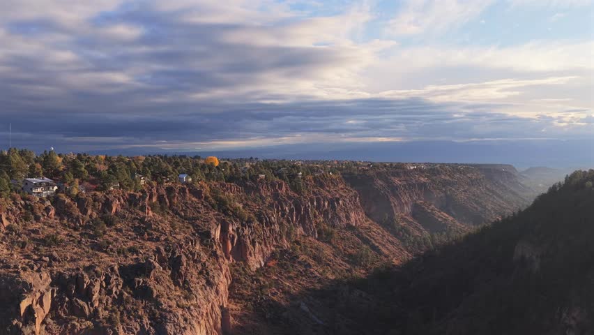 Dynamic aerial rise-and-pan shot revealing a sprawling southwest town built along the canyon rim. The vast gorge contrasts sharply with the nearby residential architecture at sunrise.