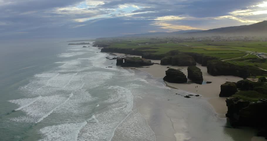 High-angle drone view of the rugged coastal cliffs of Playa de las Catedrales. The footage highlights the Cantabrian Sea and the eroded slate formations of this natural landkmark in Galicia.