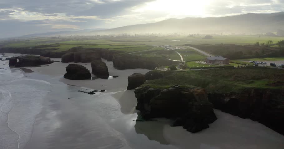 Aerial drone shot of the iconic natural arches and marine caves of Playa de las Catedrales in northern Spain. The video captures geological formations of this unique coastal scenery.