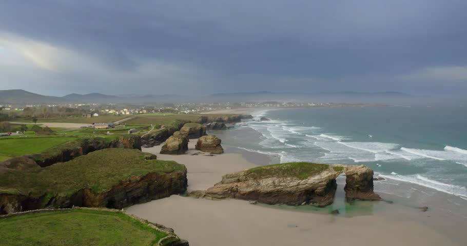 Stunning aerial drone footage of Playa de las Catedrales in Ribadeo, Galicia, Spain. Panoramic view of its unique sea arches, slate cliffs and rock formations sculpted by the Cantabrian Sea. 