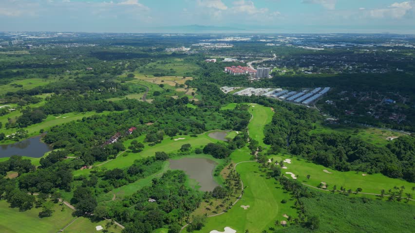 A push aerial moving across manicured fairways and tropical greenery, gradually revealing the distant horizon and urban skyline blending with natural landscapes in Calamba Laguna, Philippines