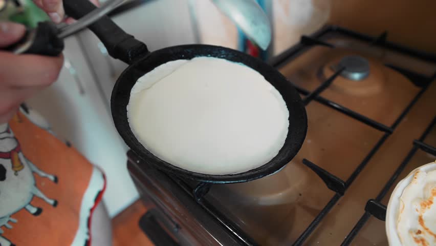 A guy is frying pancakes in a frying pan standing in the kitchen by the gas stove. Close-up shooting