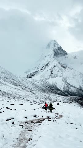 Himalayas under the clouds, majestic views of the snowy mountains, view of two climbers walking along a snowy mountain route, mountain range covered with white snow.