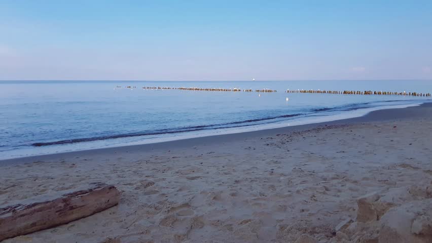 Serene seaside landscape with calm coastal surf water waves rolling on empty sand beach of Baltic sea shore under clear blue sky at cold cloudy morning. No people desolate seascape natural background.
