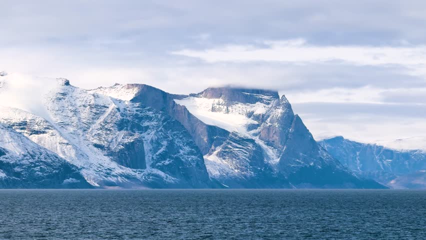 Breathtaking cliffs rise majestically above calm waters on a summer day. The clear sky showcases the beauty of the Arctic landscape with snow-capped peaks.