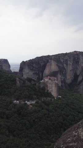 Vertical aerial shot of the Monastery of Rousanou perched on Meteora cliffs, highlighting the distinctive geological formations and rugged landscape.