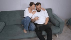 Joyful couple lounging on comfortable home sofa, sharing laptop and using credit card while enjoying seamless online shopping experience together - Powered by Shutterstock - Get 15% off with code: PIKWIZARD15