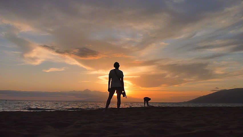 Model released woman stands and watches sunset on beach in Hawaii.