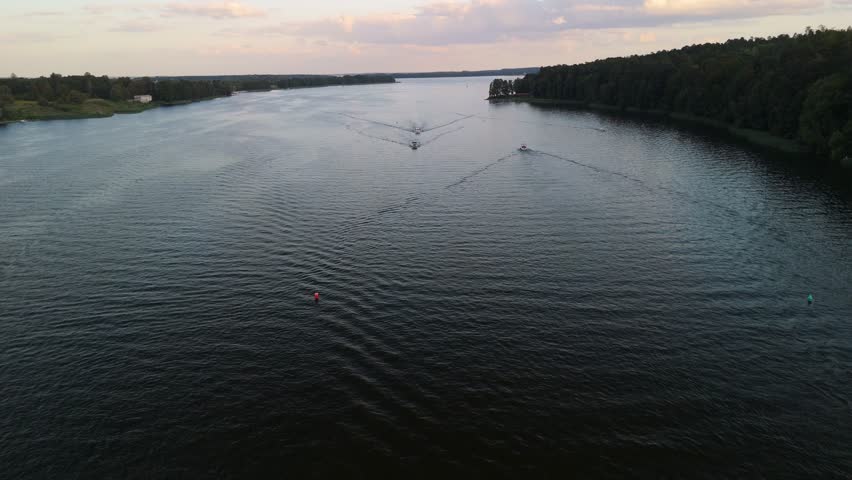 Aerial view of calm lake waters in Mikołajki at sunset, with soft waves and distant shorelines under warm evening light.