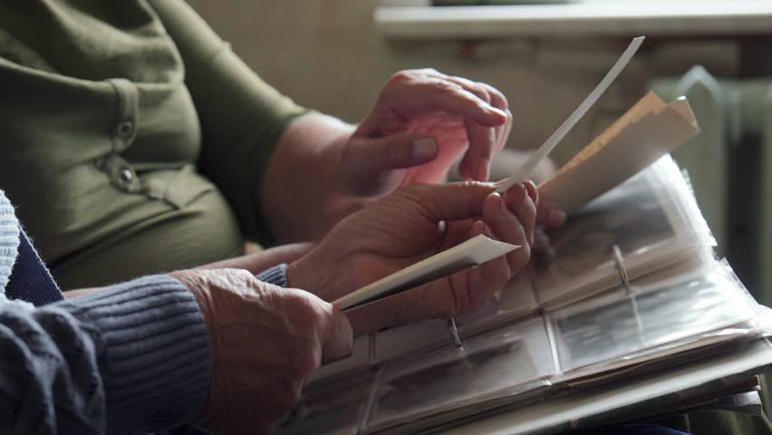 Seniors fondly viewing photographs. Wrinkled fingers gently turning pages of treasured keepsake album. Two aged adults sharing nostalgic moments as they explore their old picture collection together