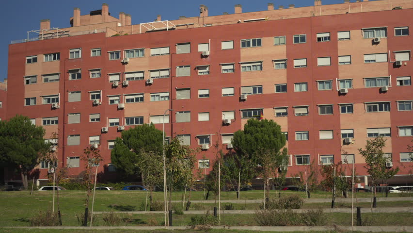 Spain, Madrid, 11 27 2025, Red brick residential building facade on a sunny day with a public park in the foreground